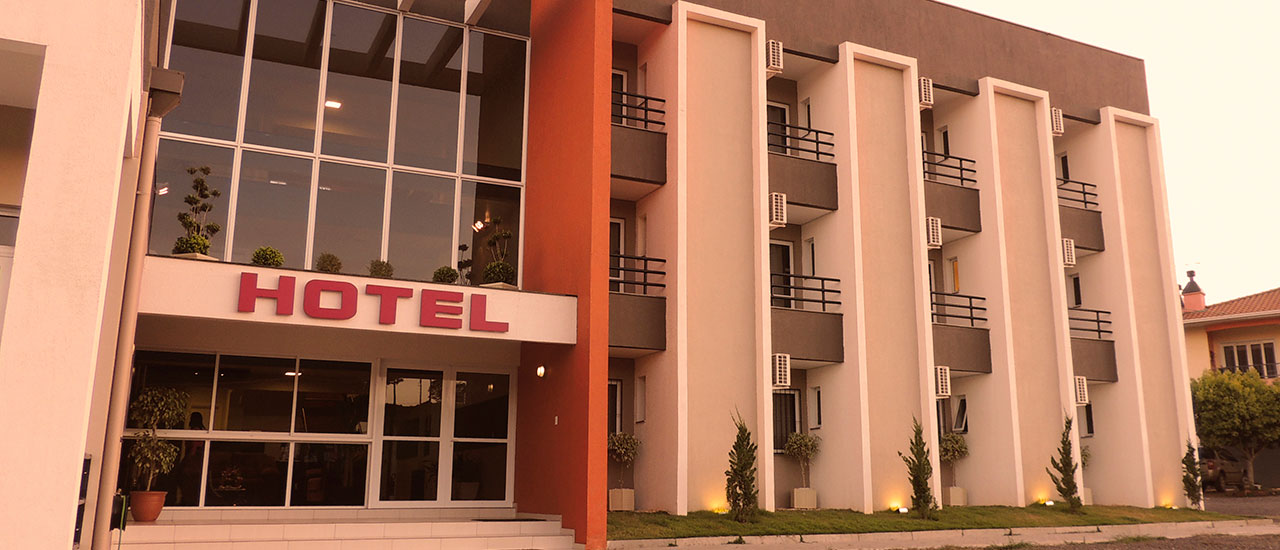Entrada do Gaúcho Hotel, com o letreiro HOTEL sobre a fachada de vidro.