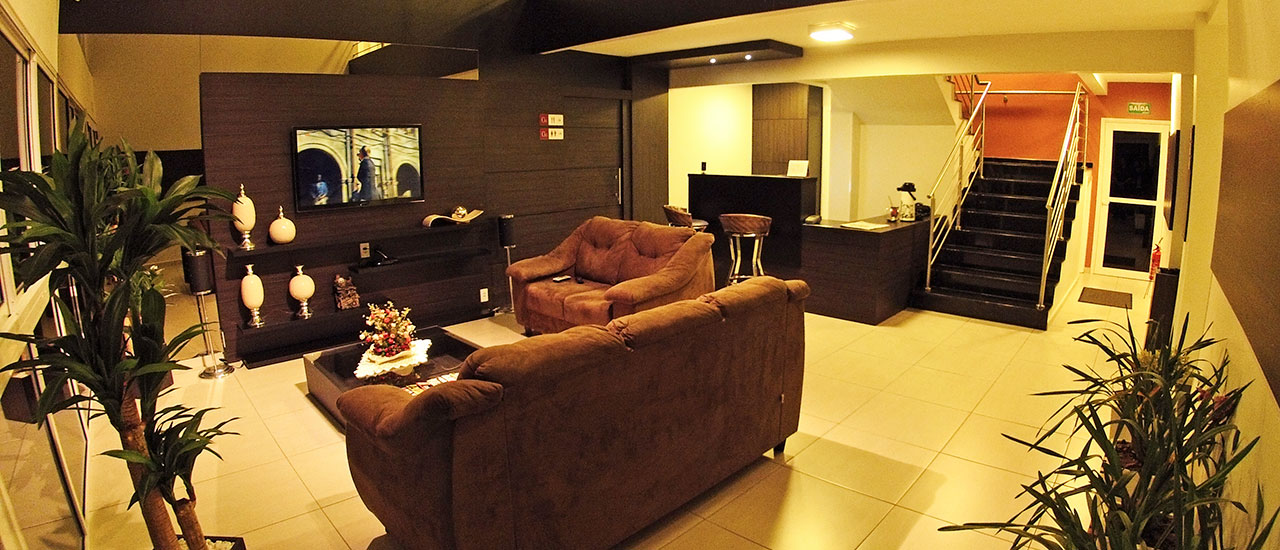 Lobby do Gaúcho Hotel, com sofás, TV e recepção.